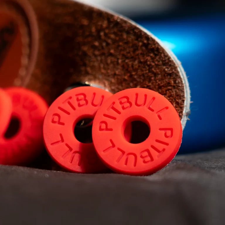 Close-up of bright red circular silicone tags with a central hole and raised text around the edge, resting beside a brown textured surface. ขายราคาพิเศษ