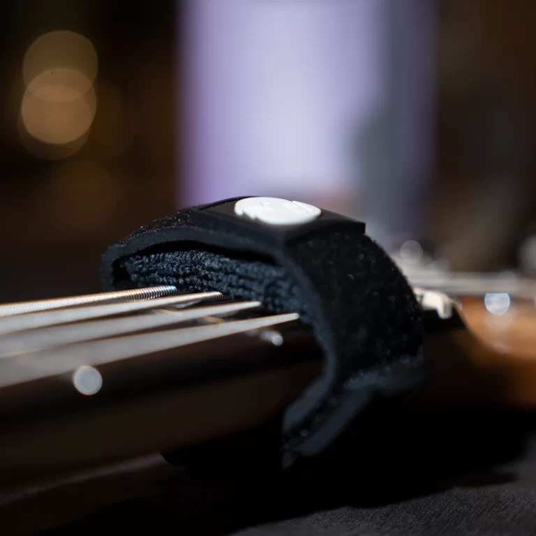 Close-up of a guitar bridge with a black strap lock and metallic strings in the foreground, shallow depth of field in the background. ขายราคาพิเศษ