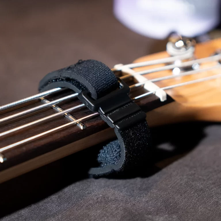 Close-up of a black fabric strap secured with a strap lock to a bass guitar neck, showing strings and wood grain. ขายราคาพิเศษ