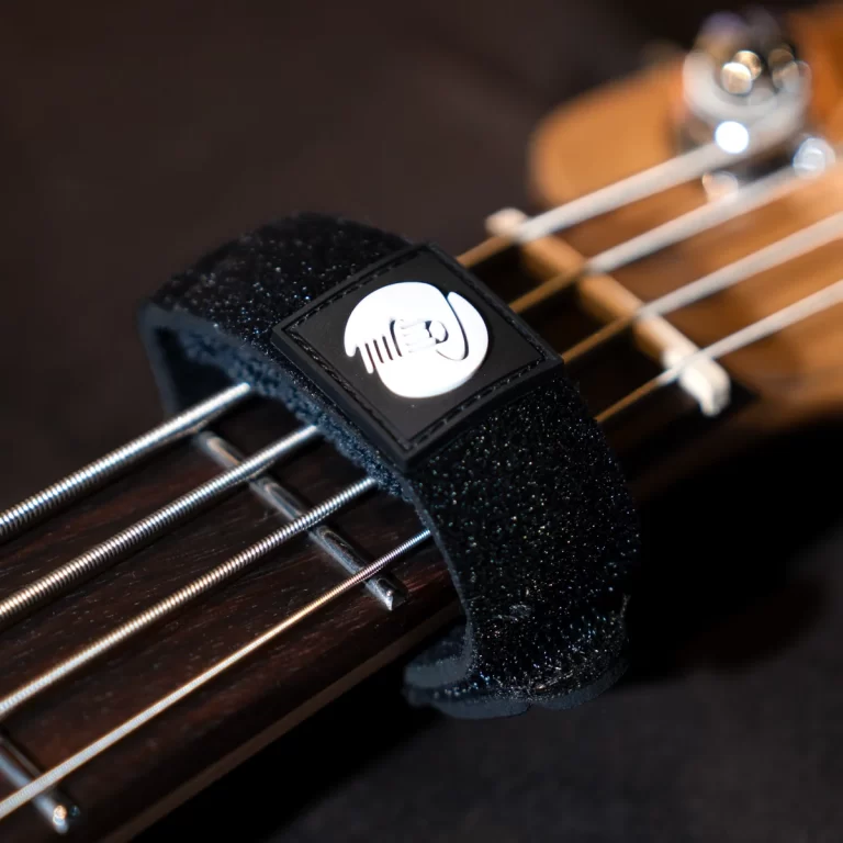 Close-up of a bass guitar neck with a black foam strap lock and a white circular logo, strings running along the fretboard. ขายราคาพิเศษ
