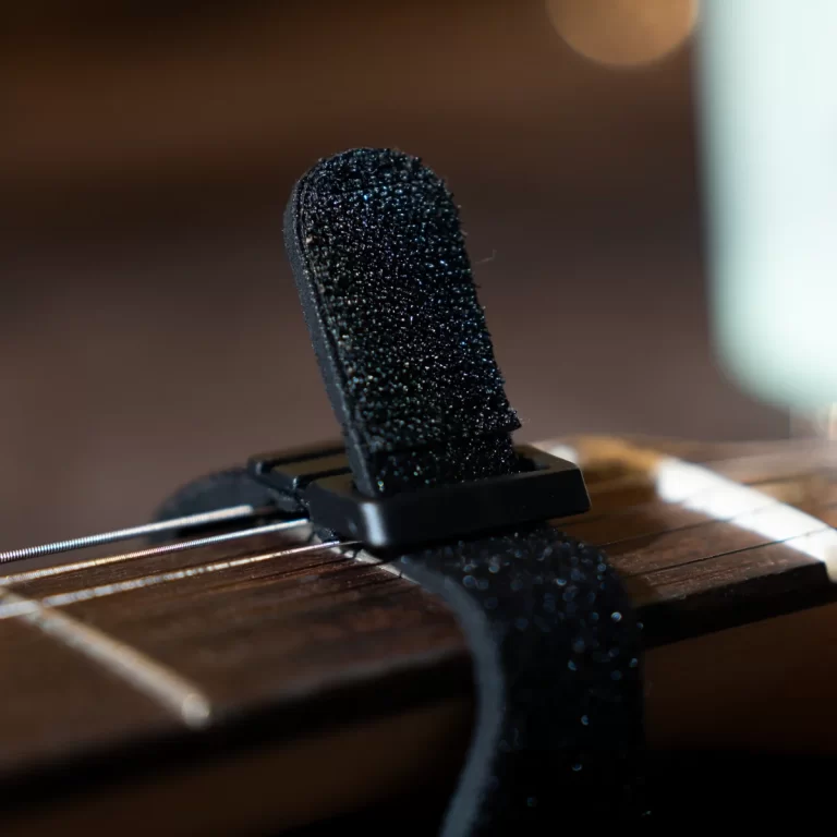 Close-up of a black fuzzy guitar strap attached to a wooden guitar body near the neck area, showing the strap lock. ขายราคาพิเศษ