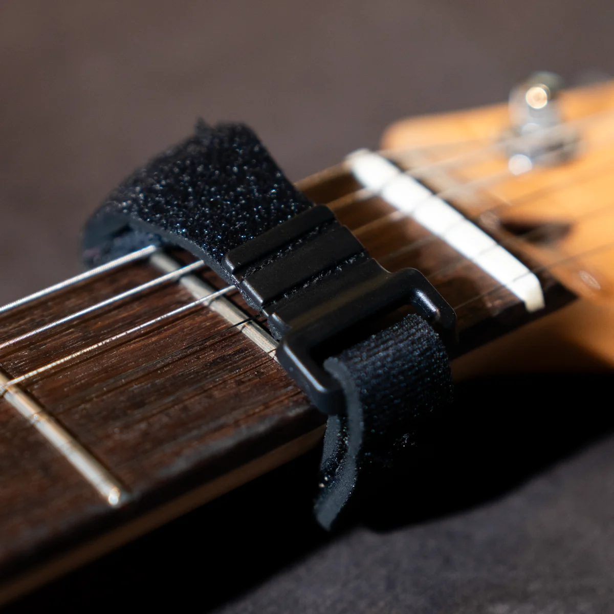 Close-up of a black strap lock attached to a guitar neck, with strings and frets visible nearby.