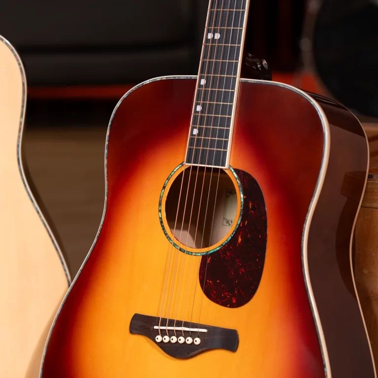 Sunburst acoustic guitar with a dark tortoiseshell pickguard and six strings, resting upright against another guitar. ขายราคาพิเศษ