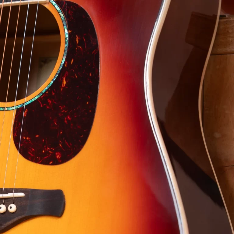 Close-up of a sunburst acoustic guitar, showing the soundhole, tortoiseshell pickguard, and curved body edges with strings across the bridge. ขายราคาพิเศษ