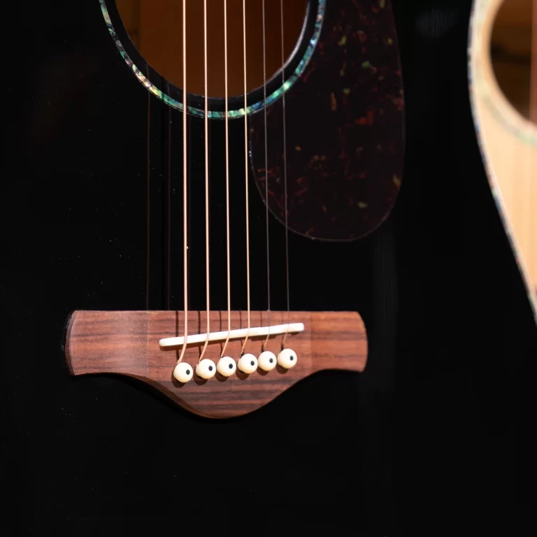 Close-up of a black acoustic guitar's bridge with six white bridge pins and steel strings. ขายราคาพิเศษ