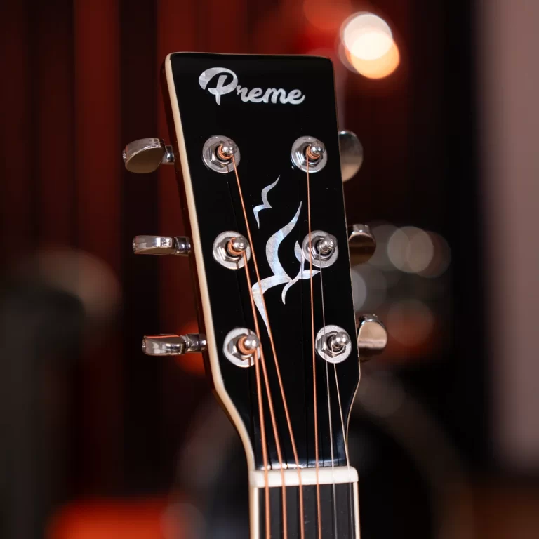 Close-up of a black guitar headstock with six chrome tuning pegs, copper strings, and a silver Preme logo with a decorative flame motif on the surface. ขายราคาพิเศษ