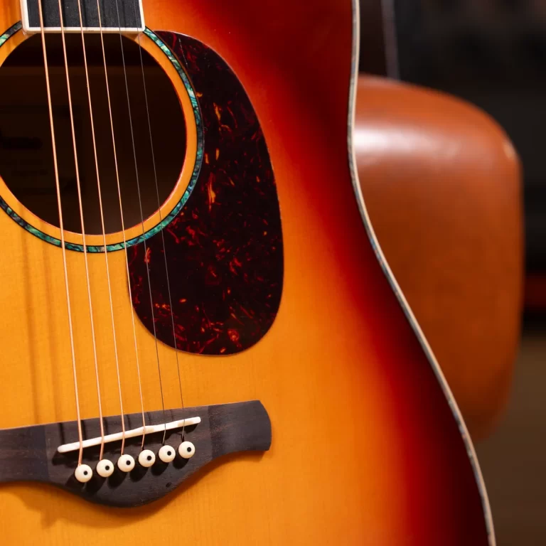 Close-up of an acoustic guitar’s body: sunburst finish, soundhole with turquoise rosette, and six strings over the bridge. ขายราคาพิเศษ