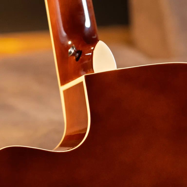 Close-up of an acoustic guitar's body and neck join, showing glossy brown wood, cream binding, and a white edge detail. ขายราคาพิเศษ