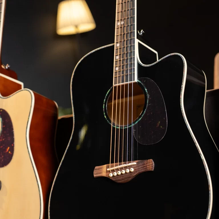 Close-up of a glossy black acoustic guitar with white binding, soundhole, and pickguard; another guitar with a natural wood finish visible to the left in a dim room. ขายราคาพิเศษ