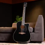 Black acoustic guitar with a cutaway leaning against a brown sofa in a dim living room. ขายราคาพิเศษ