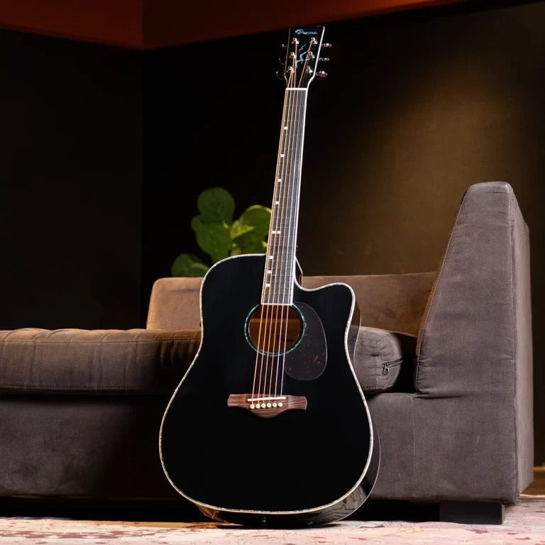 Black acoustic guitar with a cutaway leaning against a brown sofa in a dim living room. ขายราคาพิเศษ