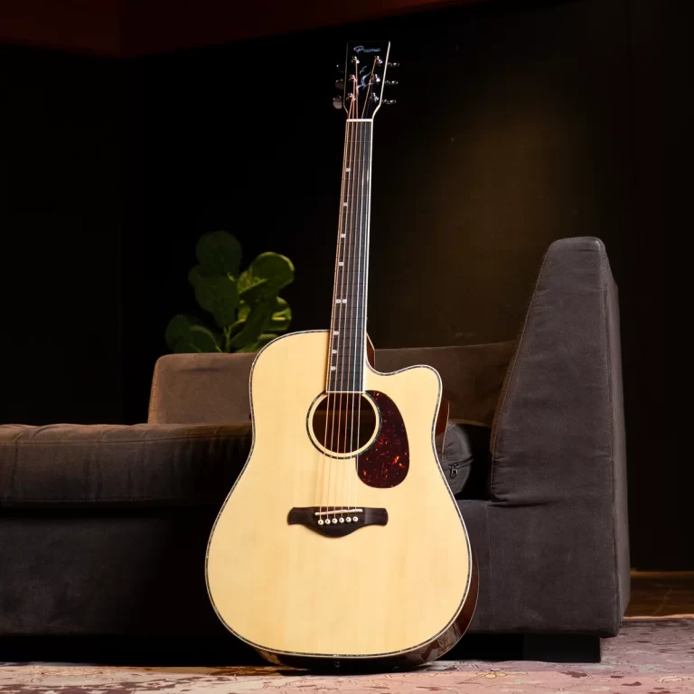 Light-colored acoustic guitar leaning against a dark sofa in a dim room. ขายราคาพิเศษ