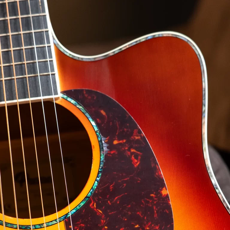 Close-up of an orange sunburst acoustic guitar showing the soundhole, teal rosette, and tortoiseshell pickguard with strings across the neck. ขายราคาพิเศษ