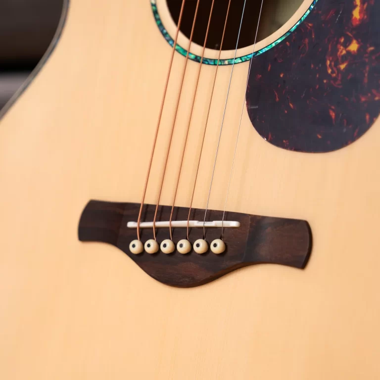 Close-up of an acoustic guitar showing strings over the wooden bridge and soundhole area on a light wood body. ขายราคาพิเศษ