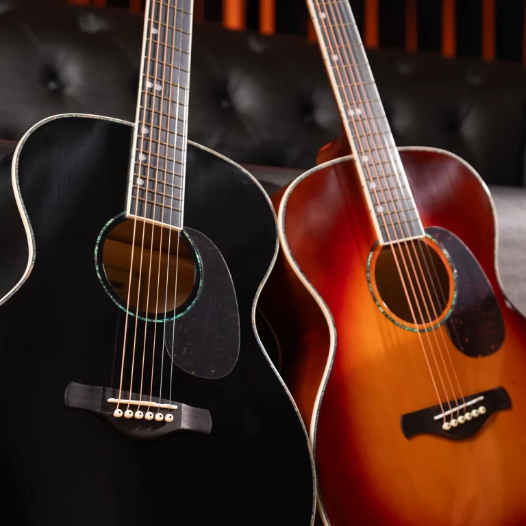 Two acoustic guitars leaning together: a black guitar on the left and a sunburst guitar on the right in a dim setting. ขายราคาพิเศษ