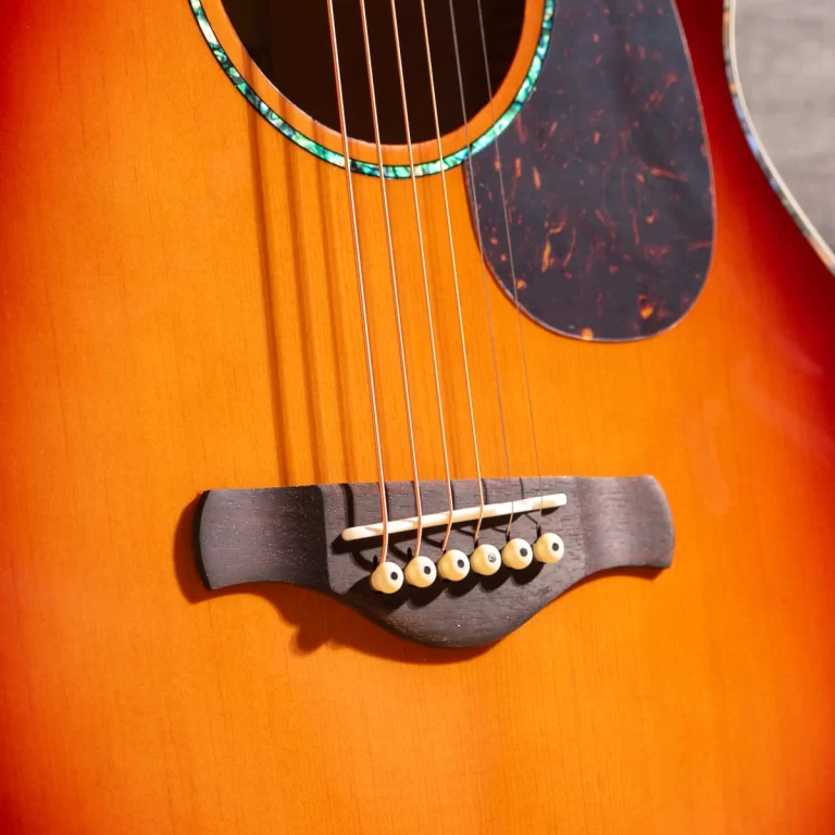 Close-up of an acoustic guitar bridge with six strings anchored to white bridge pins on an orange wood finish. ขายราคาพิเศษ