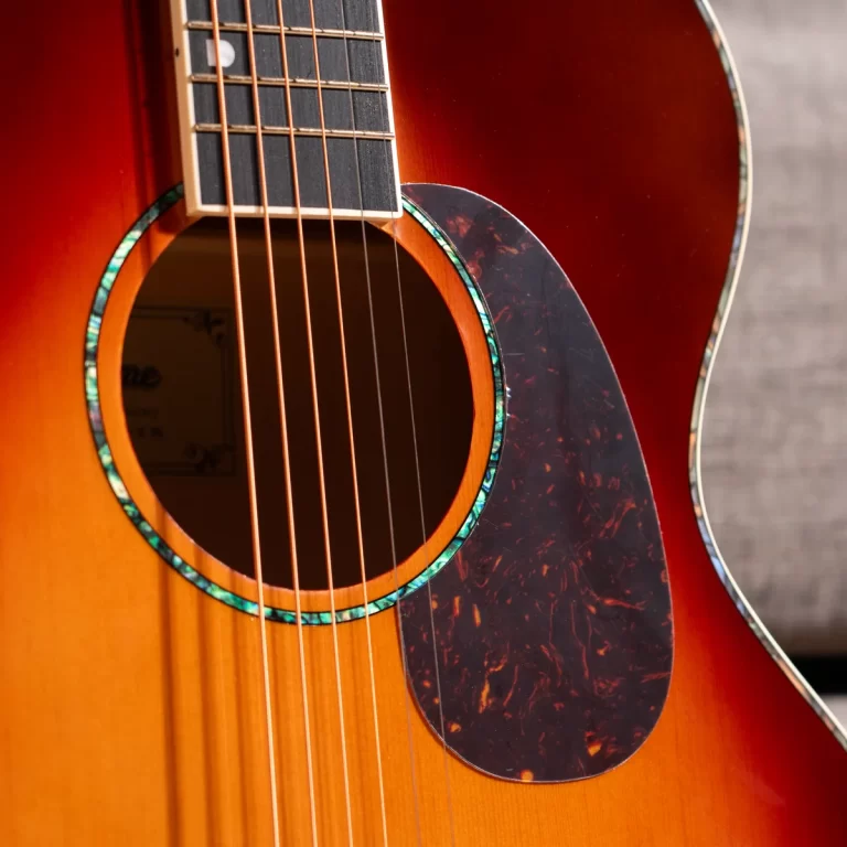 Close-up of an acoustic guitar focusing on the sound hole, sunburst finish, and turquoise-inlaid rosette with six strings crossing the fretboard area. ขายราคาพิเศษ