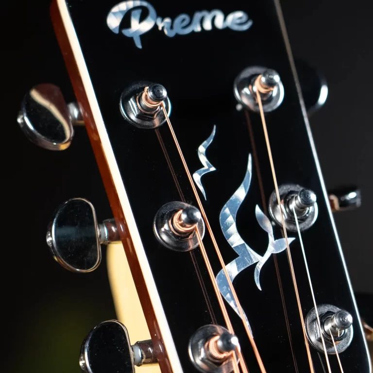 Close-up of a black guitar headstock with silver tuning pegs, copper strings, and a silver flame inlay on the surface. ขายราคาพิเศษ