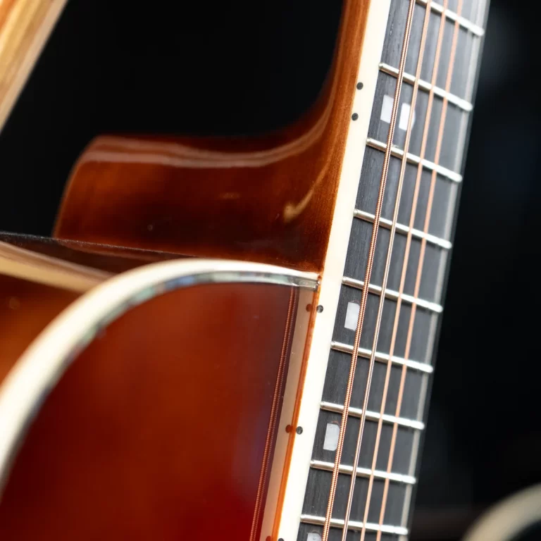 Close-up of an acoustic guitar neck and fretboard, showing frets, copper strings, and a sunburst body. ขายราคาพิเศษ