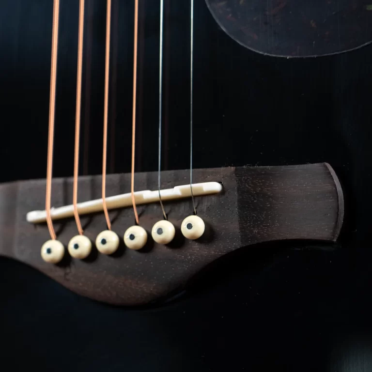 Close-up of a guitar bridge with nylon and copper strings, white bridge pins, and a white saddle against a dark wooden body. ขายราคาพิเศษ