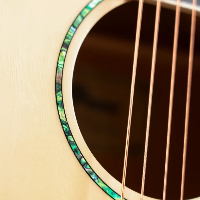 Close-up of an acoustic guitar soundhole with a green mother-of-pearl rosette and copper strings passing over the opening ขายราคาพิเศษ