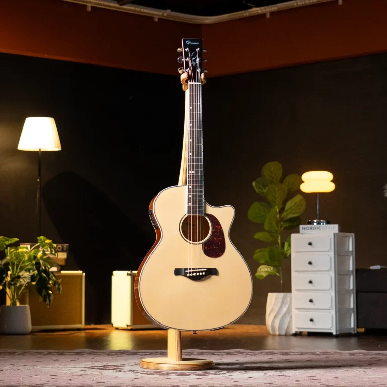 Cream-colored acoustic guitar on a stand in a cozy studio setting with plants and warm lighting in the background. ขายราคาพิเศษ