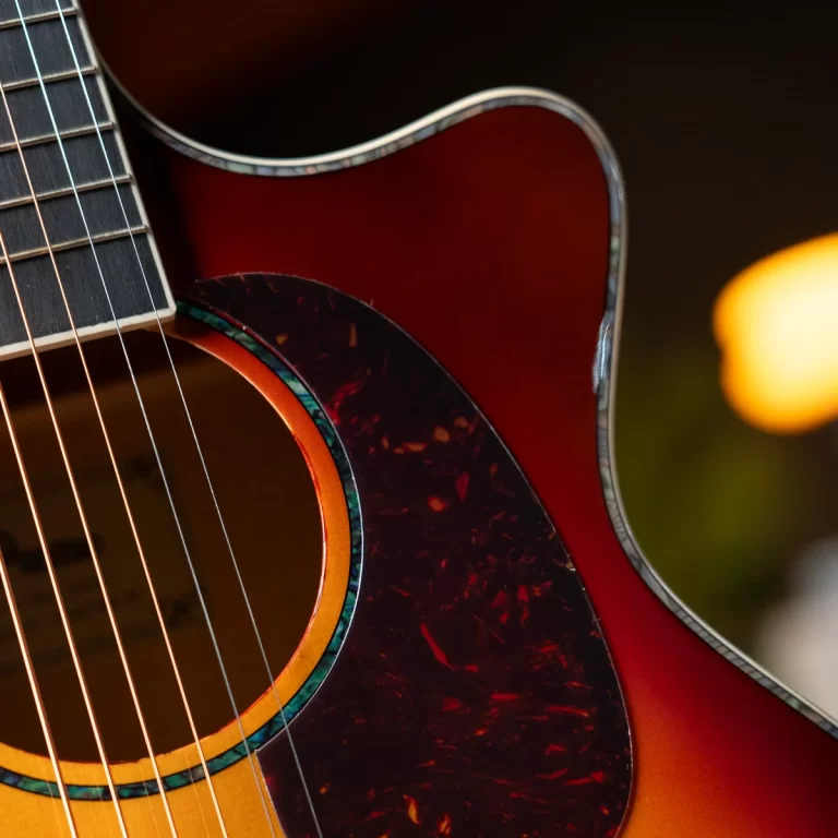 Close-up of an acoustic guitar showing strings, soundhole, and a red tortoiseshell pickguard end. ขายราคาพิเศษ