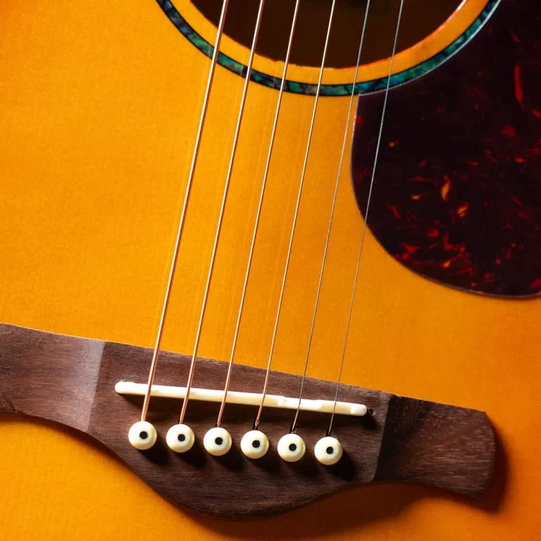 Close-up of six guitar strings over the bridge of an acoustic guitar, with a light wooden top and visible saddle pins. ขายราคาพิเศษ