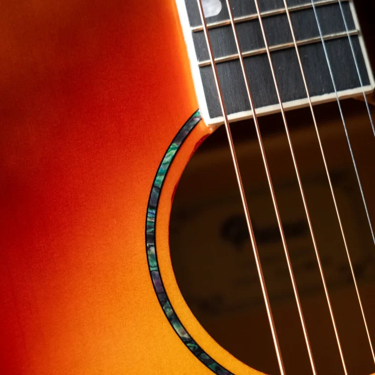 Close-up of an orange sunburst acoustic guitar with a blue-green rosette around the soundhole and six strings. ขายราคาพิเศษ