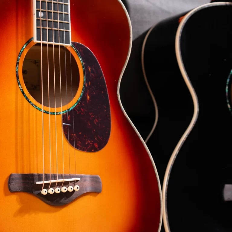 Close-up of an orange sunburst acoustic guitar showing strings, soundhole, and a dark tortoiseshell pickguard with another guitar in the background only partly visible. ขายราคาพิเศษ