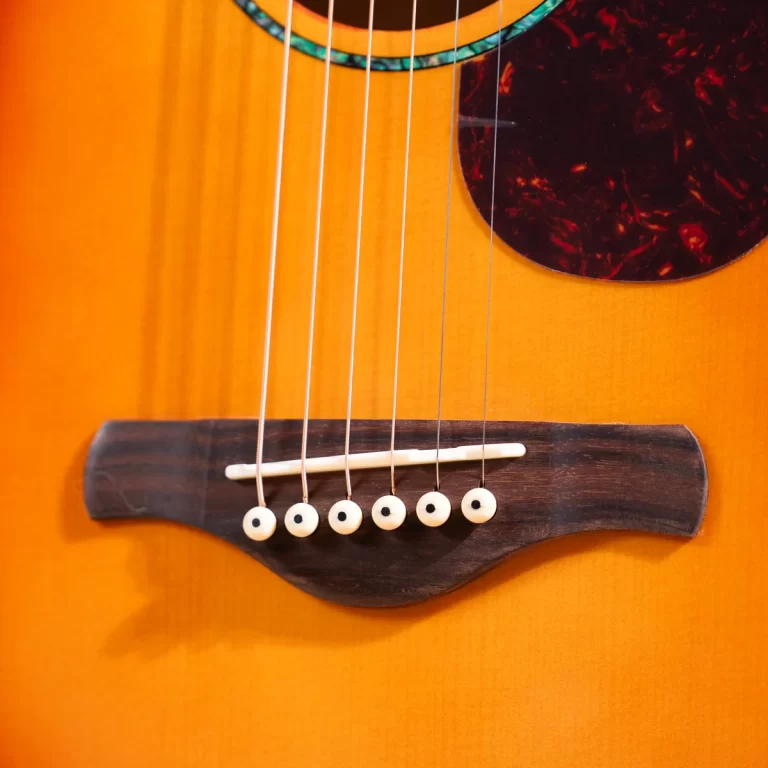 Close-up of an acoustic guitar bridge with six strings and white bridge pins on an orange finish. ขายราคาพิเศษ