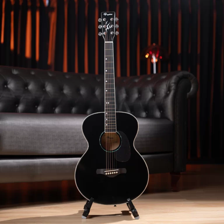 Black acoustic guitar on a stand in a dim, stylish living room with a tufted leather sofa behind it. ขายราคาพิเศษ
