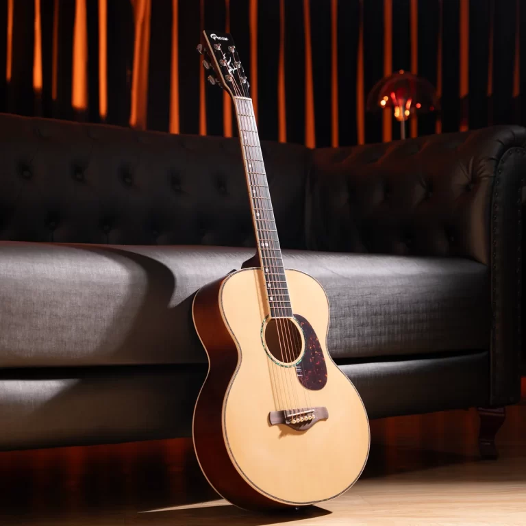 Acoustic guitar leaning on a dark tufted leather couch in a dimly lit room. ขายราคาพิเศษ