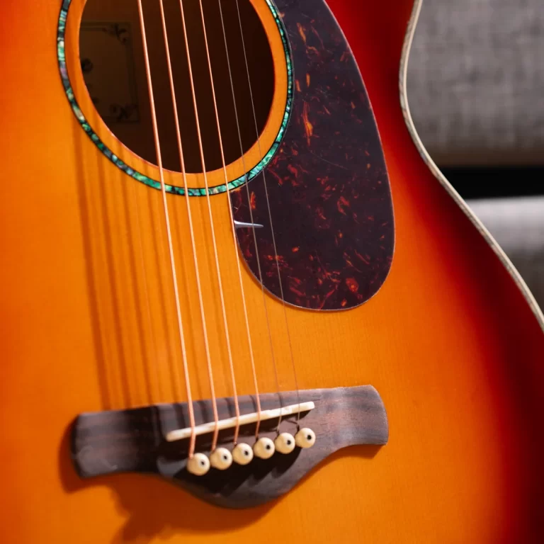 Close-up of an orange sunburst acoustic guitar showing the soundhole with turquoise rosette, six strings, and tortoiseshell pickguard. ขายราคาพิเศษ