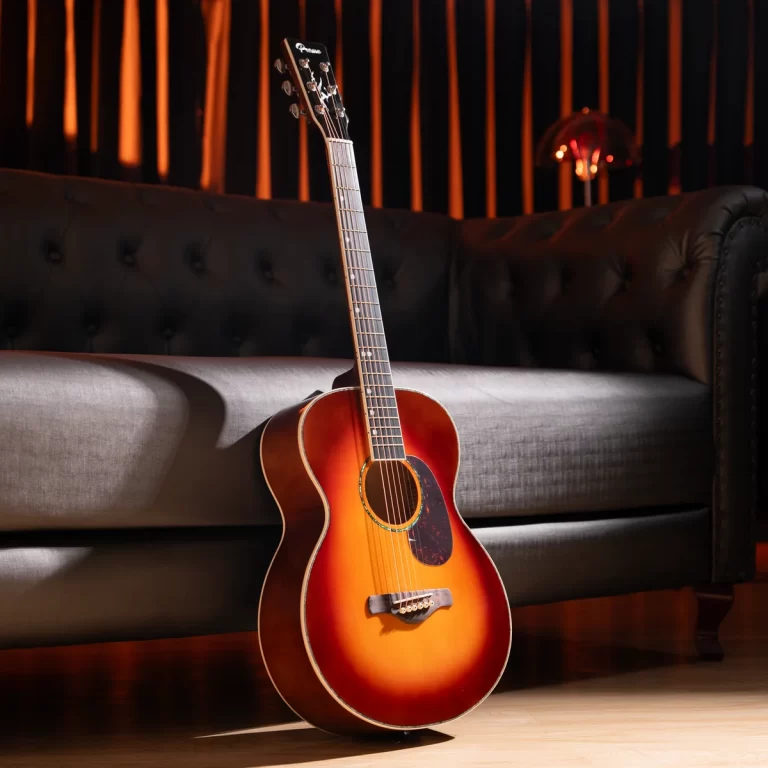 Sunburst acoustic guitar leaning against a dark tufted sofa in a warmly lit living room. ขายราคาพิเศษ