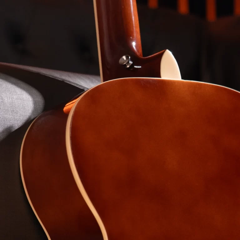 Close-up of a glossy brown acoustic guitar body and neck joint, showing white binding along the edge against a dark background. ขายราคาพิเศษ