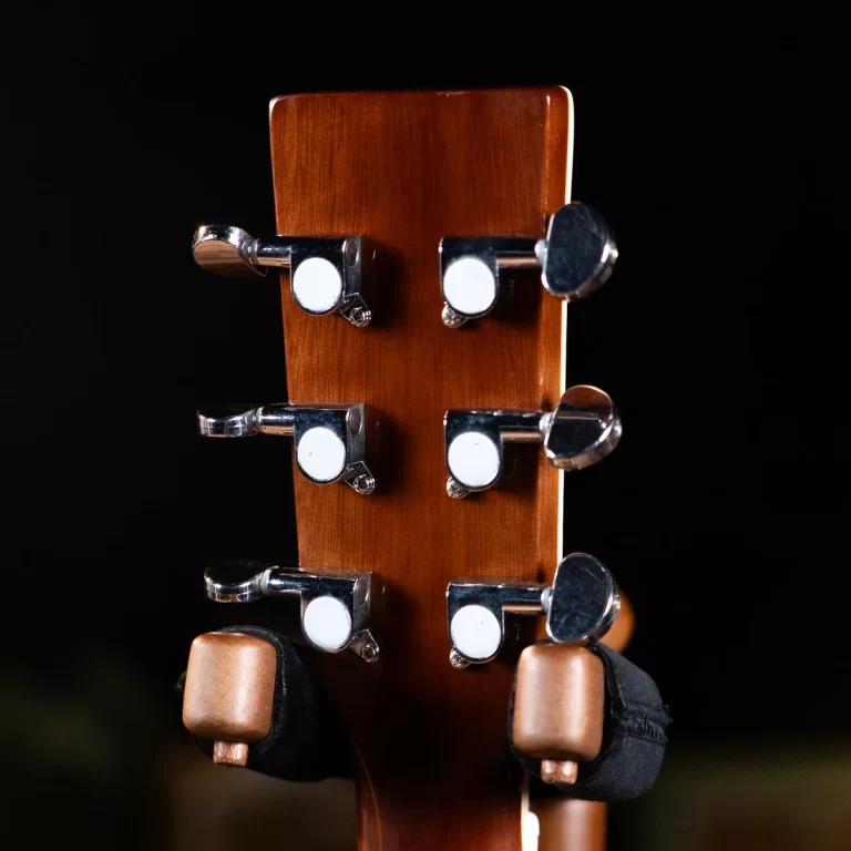 Close-up of a guitar headstock with chrome tuning pegs on a brown wood neck against a dark background. ขายราคาพิเศษ