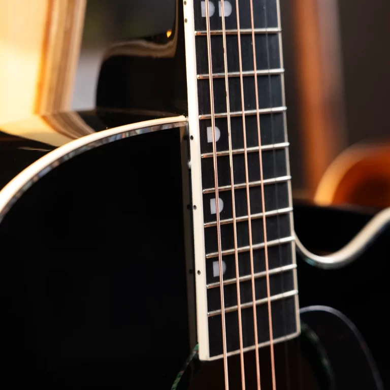 Close-up of a guitar neck and strings on a black acoustic guitar, focusing on the frets and fretboard ขายราคาพิเศษ