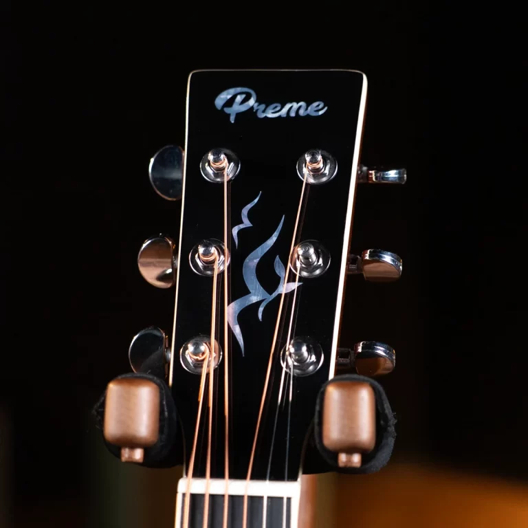 Close-up of a guitar headstock: six metal tuning pegs, copper strings, and a black glossy surface with a blue flame inlay and the 'Preme' logo at the top. ขายราคาพิเศษ