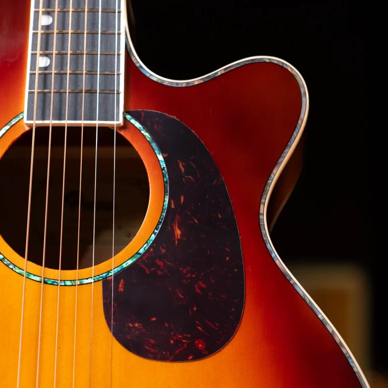 Close-up of a sunburst acoustic guitar showing strings over the soundhole and tortoiseshell pickguard in a vibrant finish. ขายราคาพิเศษ
