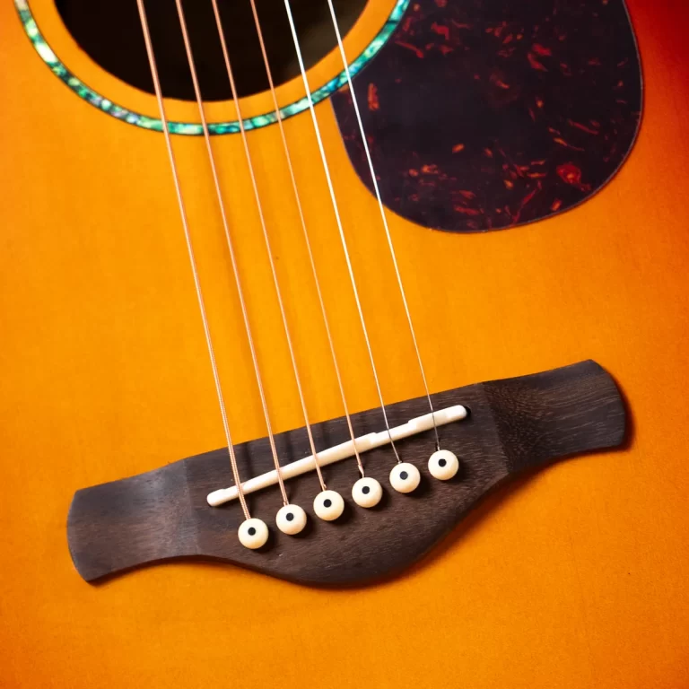 Close-up of the strings and bridge on an acoustic guitar with a warm wooden finish and tortoiseshell pickguard nearby. ขายราคาพิเศษ