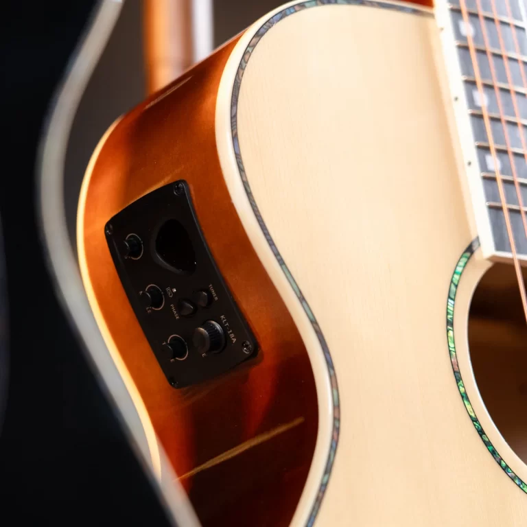 Close-up of a sunburst acoustic guitar body showing a black electronic control panel with knobs on the side. The guitar features decorative binding and a light soundboard. ขายราคาพิเศษ