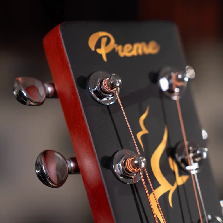 Close-up of a guitar headstock with tuning pegs and copper strings on a black and red guitar, featuring a gold logo design in the center. ขายราคาพิเศษ