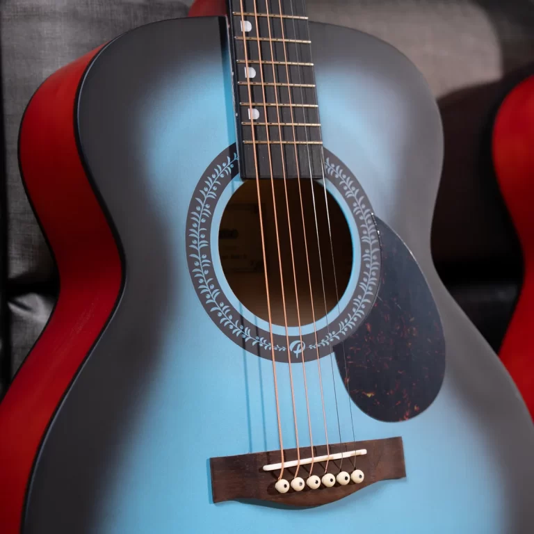 Close-up of a blue acoustic guitar with a decorative rosette around the soundhole and six strings, red sides visible in the background. ขายราคาพิเศษ