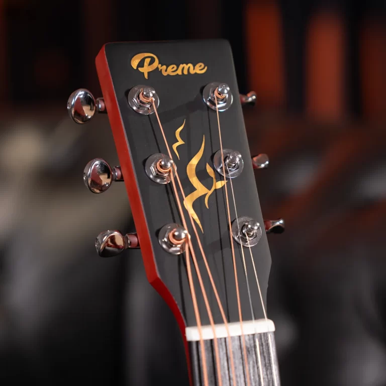 Close-up of a black guitar headstock with a gold flame logo and copper strings, tuning pegs visible. ขายราคาพิเศษ