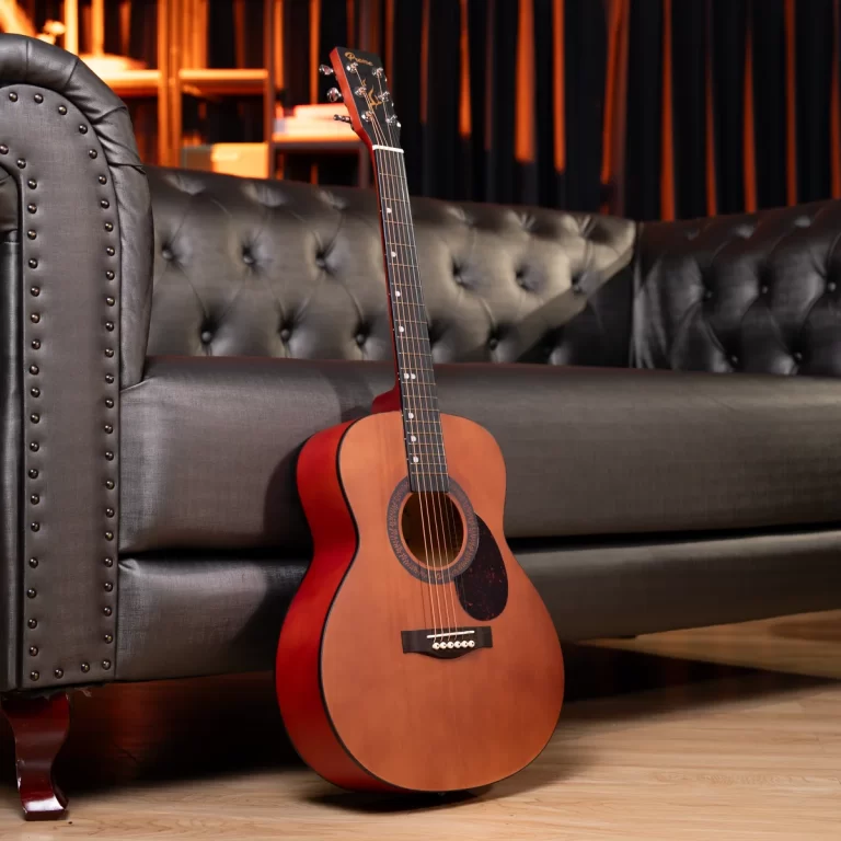 An acoustic guitar with a natural wood finish leaning against a tufted black leather couch in a warmly lit lounge. ขายราคาพิเศษ