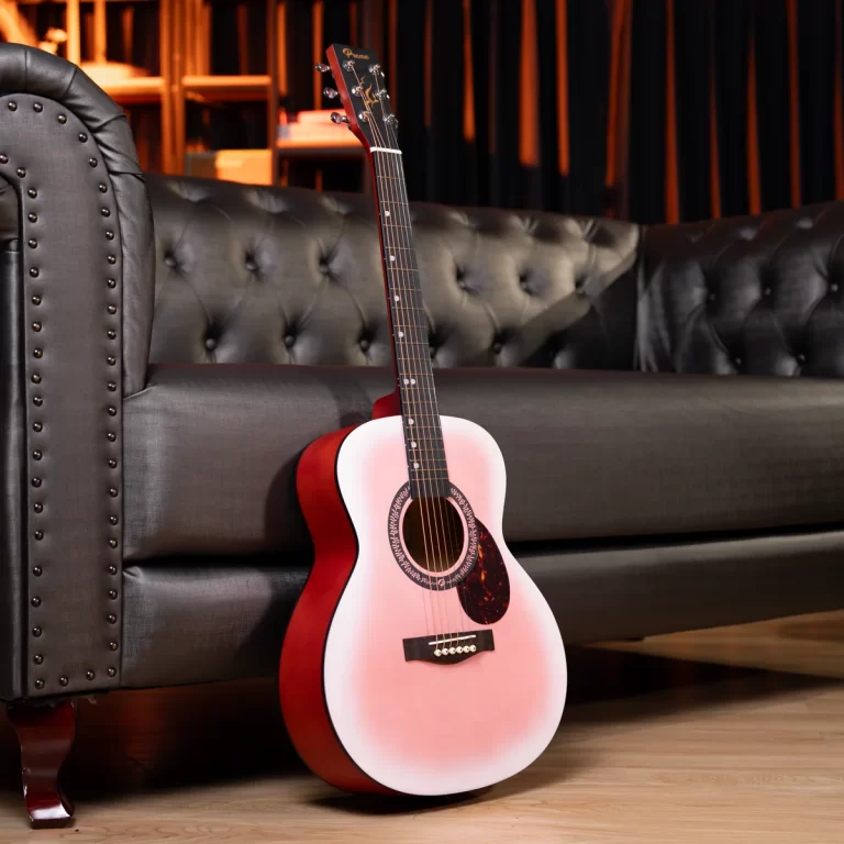 Pink acoustic guitar leaning against a dark tufted sofa in a cozy lounge setting. ขายราคาพิเศษ