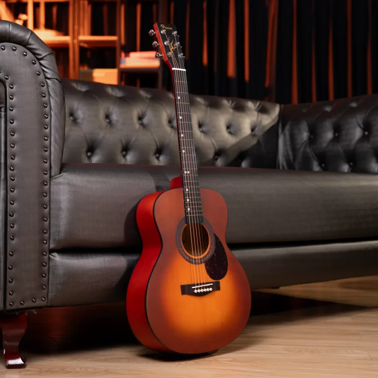 Sunburst acoustic guitar leaning against a tufted black leather sofa in a warm, stylish lounge. ขายราคาพิเศษ