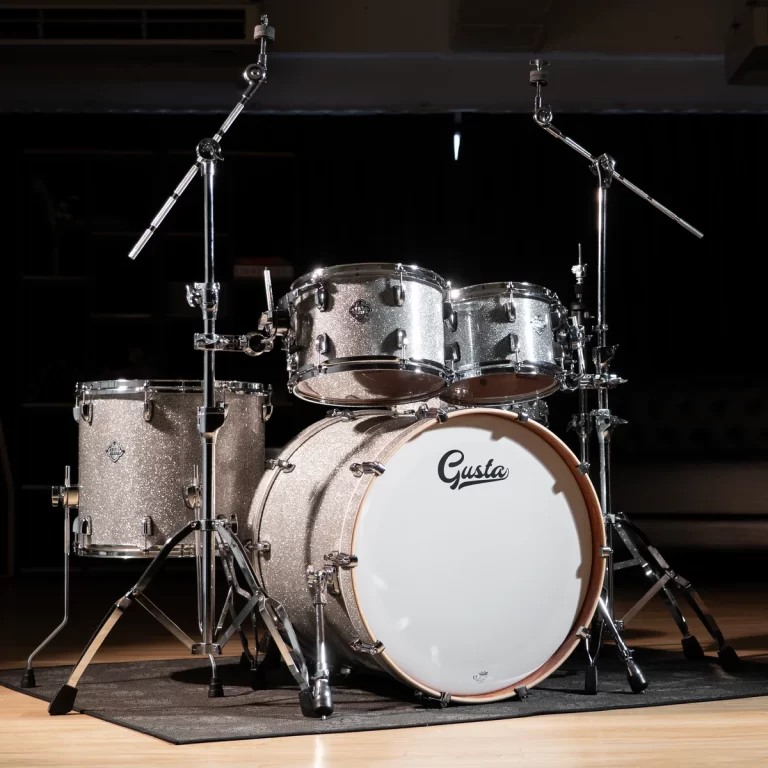 Glittery silver drum kit on a stage with a bass drum labeled 'Gusta' and multiple toms on chrome stands. ขายราคาพิเศษ