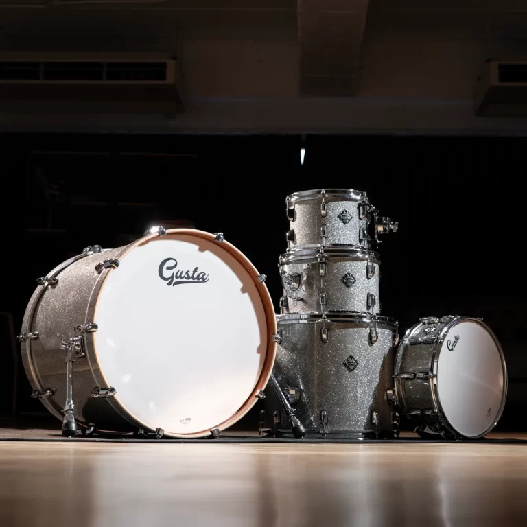 Silver glitter drum kit on a dark stage, with a large bass drum showing the 'Gusta' logo. ขายราคาพิเศษ